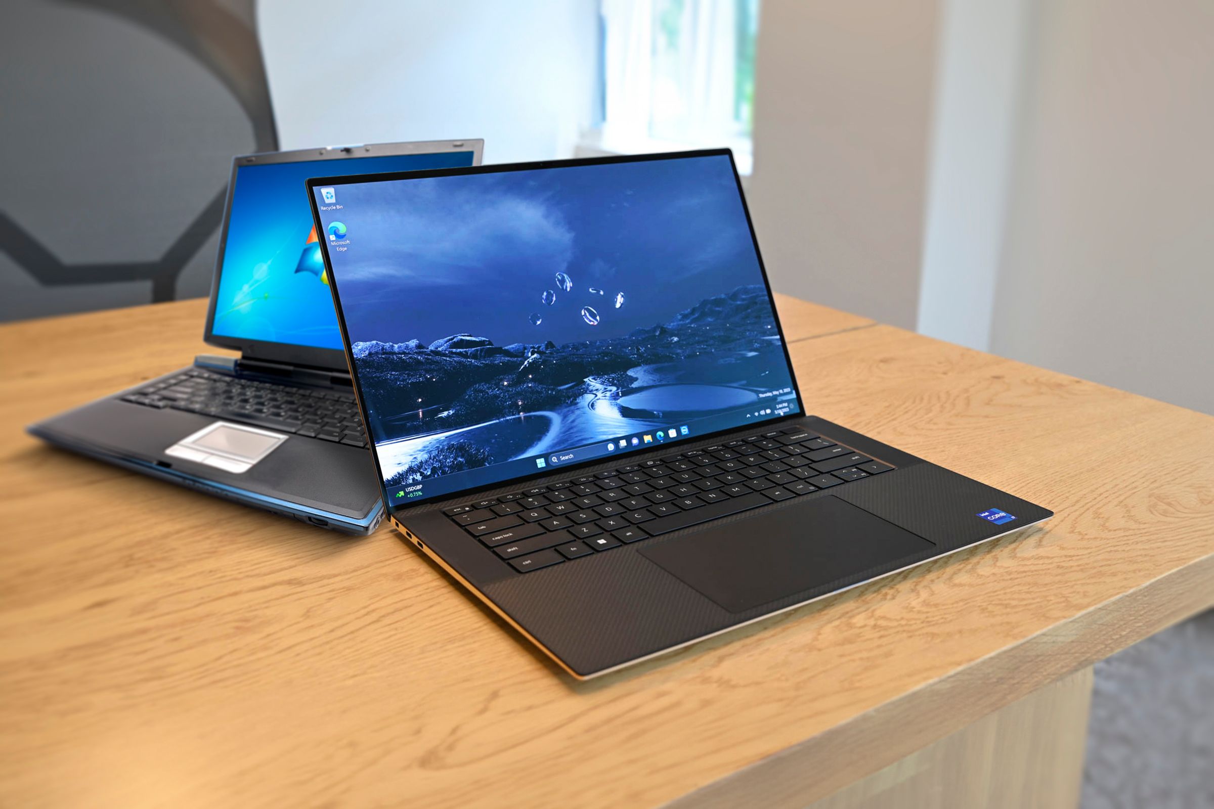 Two laptops on a wooden desk, with a modern laptop in the center of the screen and an old laptop behind it.
