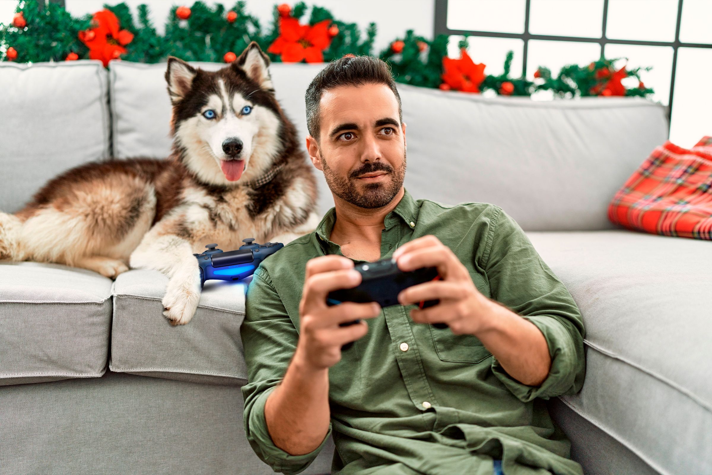 A man playing video game on the couch with his dog.