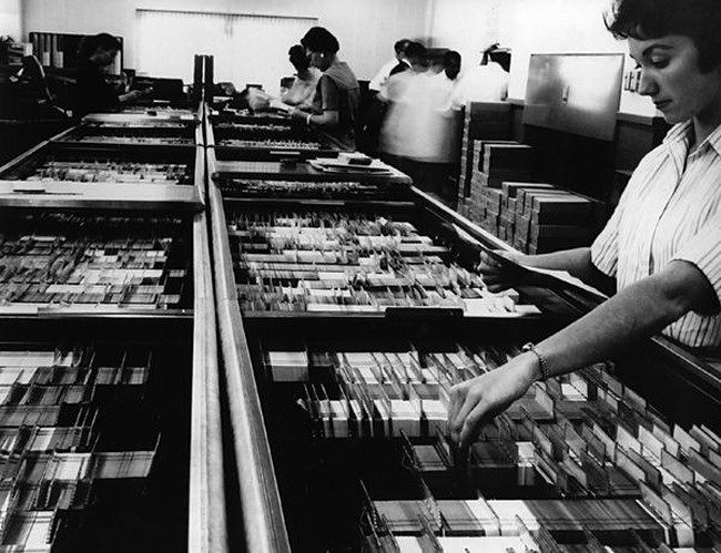 Workers pull punched cards from a tub file.
