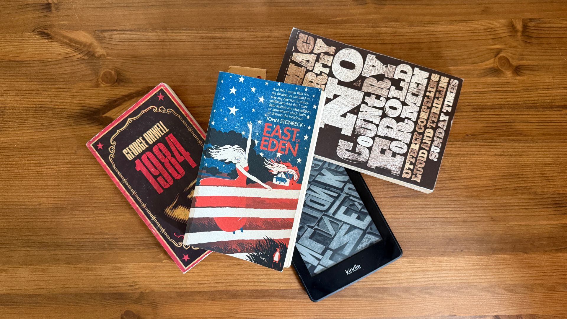 Books lying on top of a Kindle eReader on a desk.