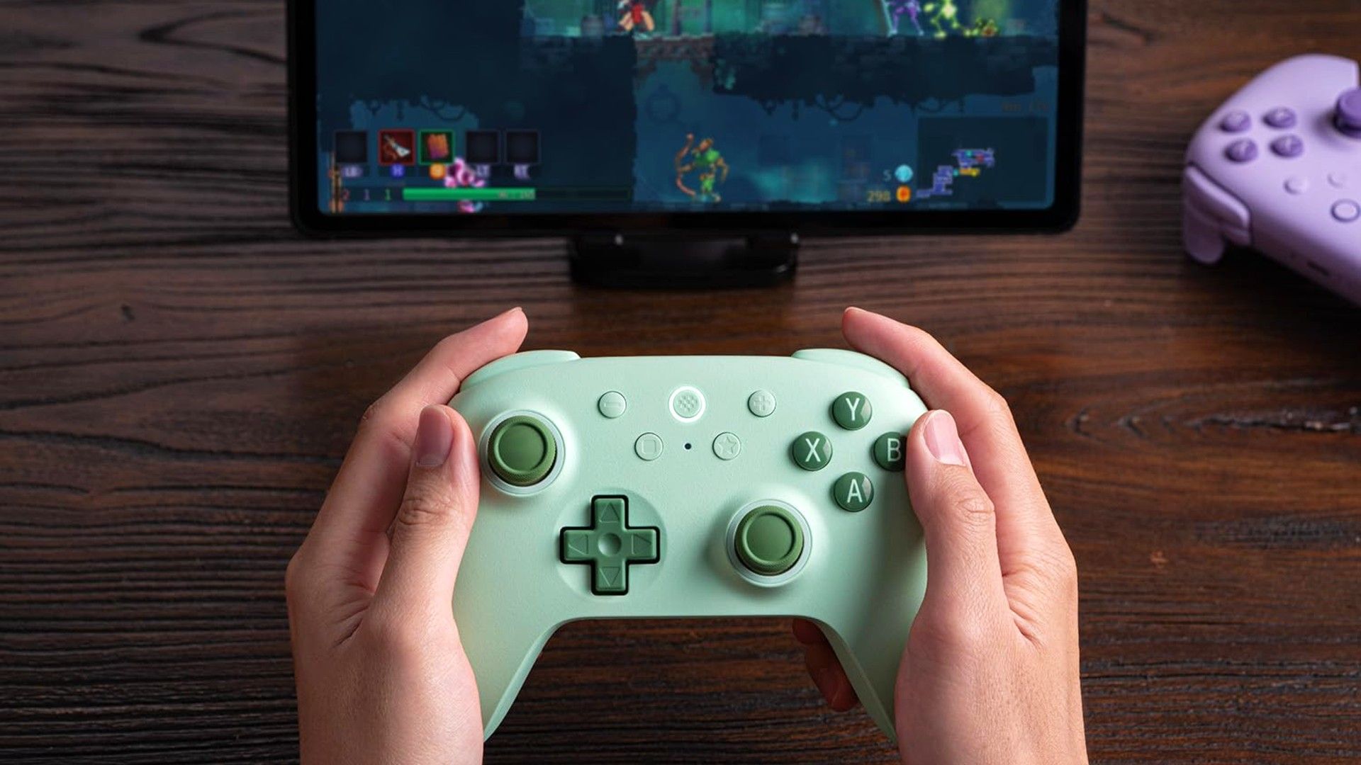 Two hands holding a 8BitDo Ultimate 2C wireless controller in front of a game being played