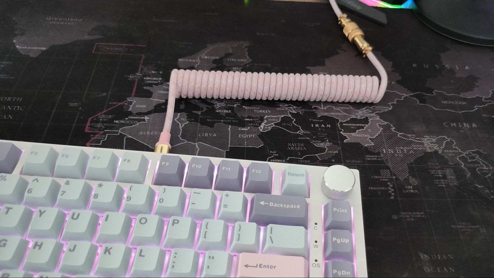 A pink coiled keyboard cable plugged into a white keyboard with light blue and purple keycaps.