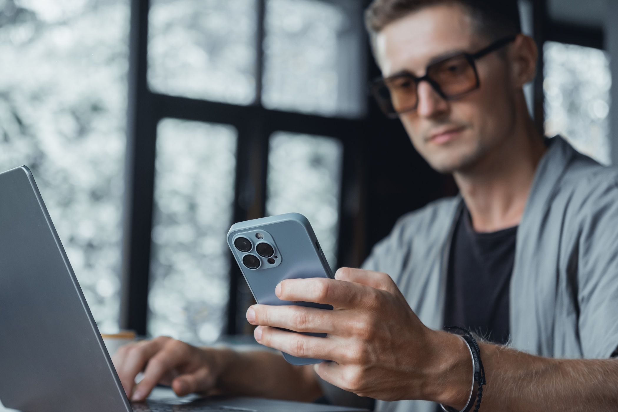 man holding iphone while looking at laptop