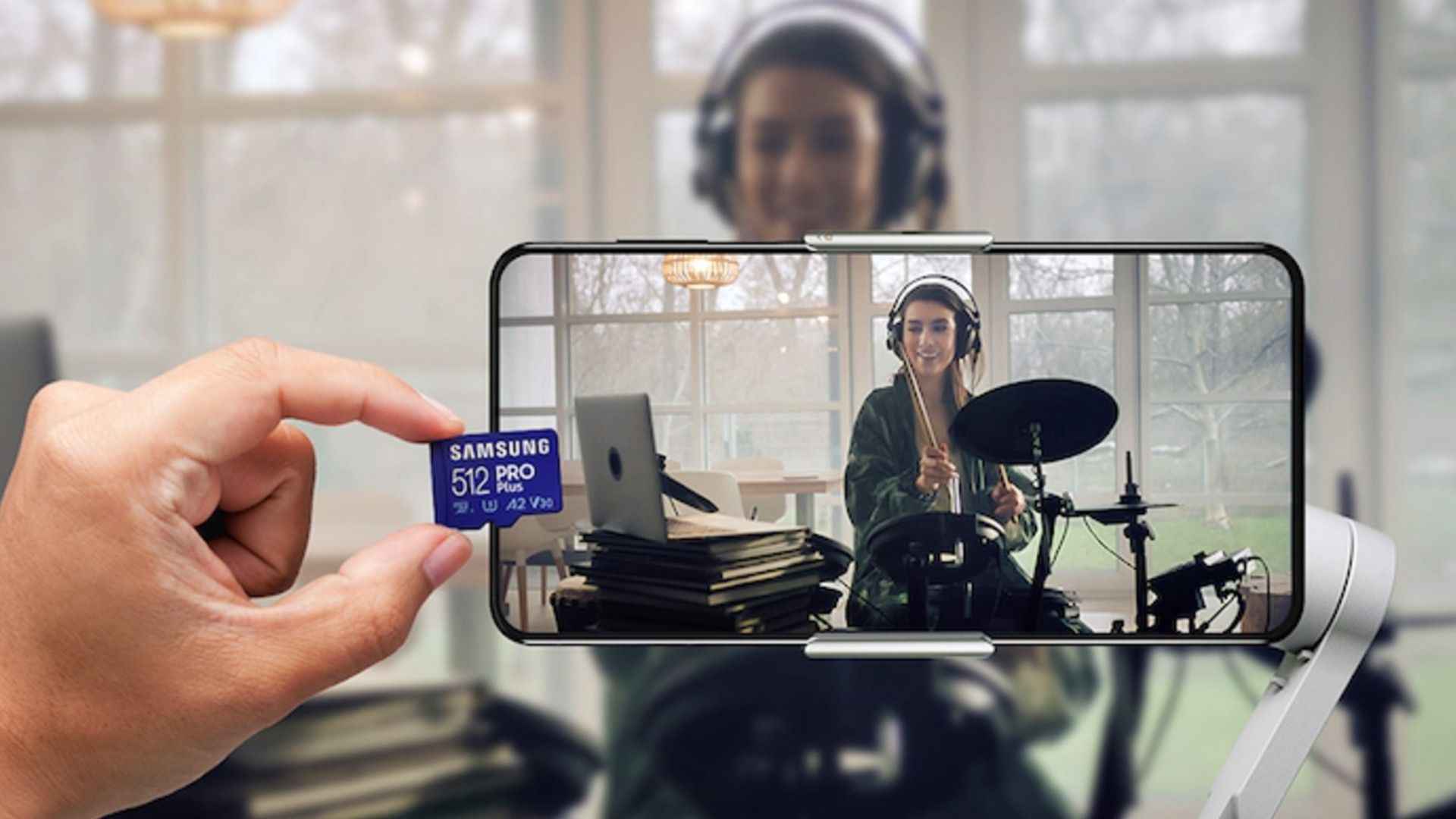 person holding samsung pro plus micro SD next toa phone taping another person playing a drum